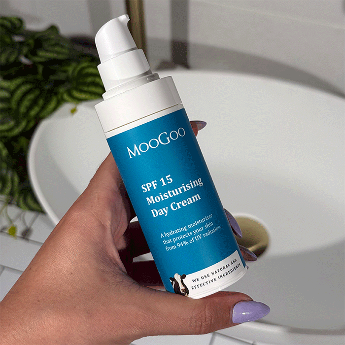 MooGoo SPF 15 Moisturising Day Cream held by person in bathroom, lightweight non-greasy formula with SPF 15 to block 94% of UV radiation daily.