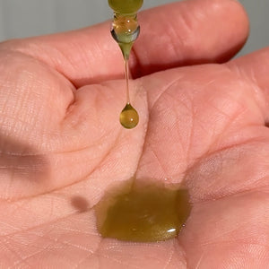 MooGoo 100% Tamanu face oil droplet falling onto hand. 