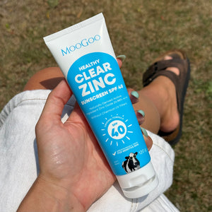 Hand holding a tube of MooGoo Clear Zinc Sunscreen SPF 40 on grass background. Without Chemical UV Filters, Zinc Oxide Based Sunscreen with broad spectrum UVA & UVB protection.