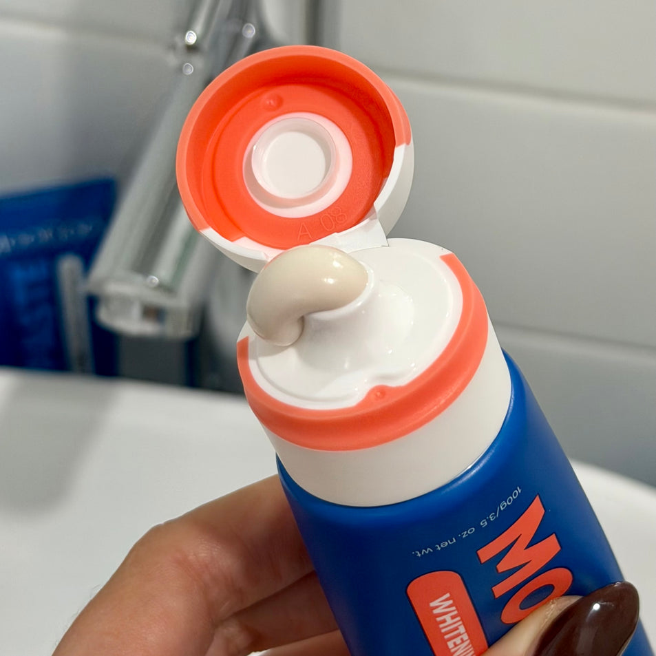 MooGoo Fluoride-Free Watermelon and Mint Whitening toothpaste tube with toothpaste being squeezed out, held by a hand.
